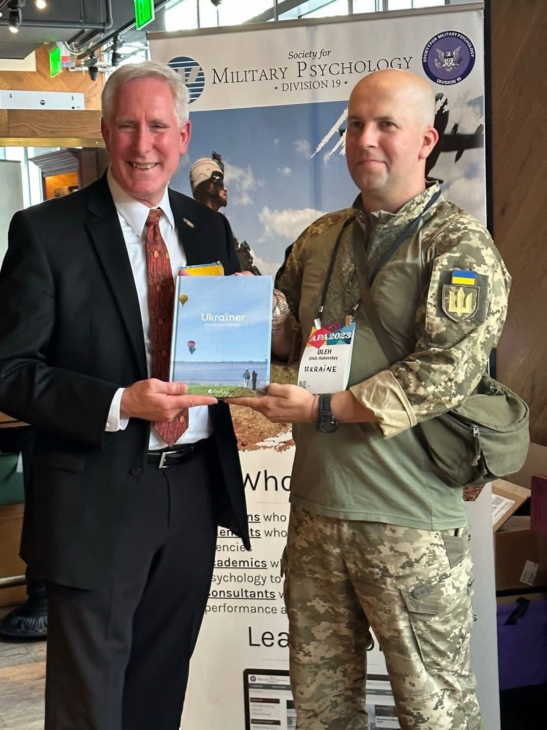 A member of the team in Ukrainian uniform presents a book about the work at a stand of the Society for Military Psychology.