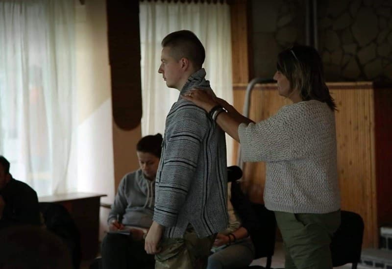 A trainer places her hands on a veteran’s shoulders while the group watches.