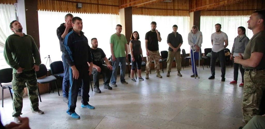 Veterans and trainers stand in a wide circle in a bright training room.
